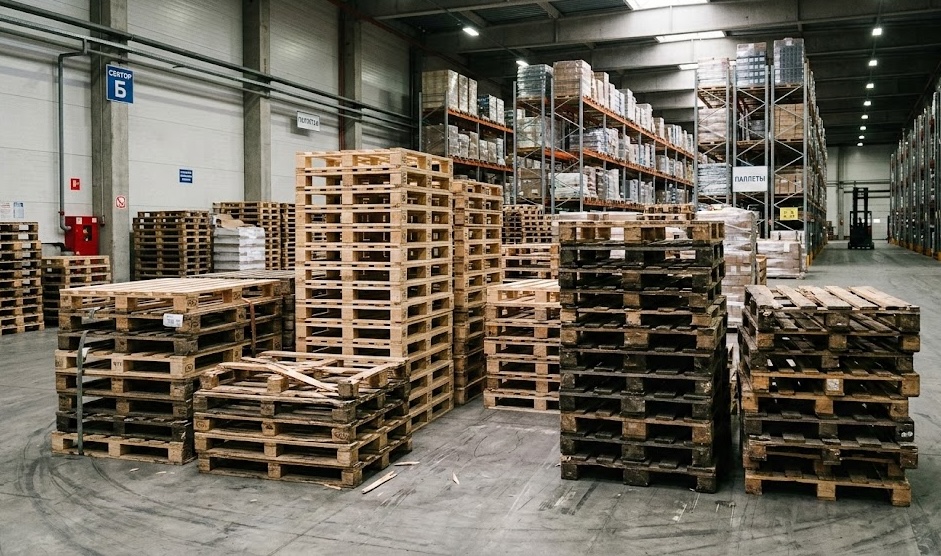 Stacked pallets in warehouse with shelving showing inventory variety